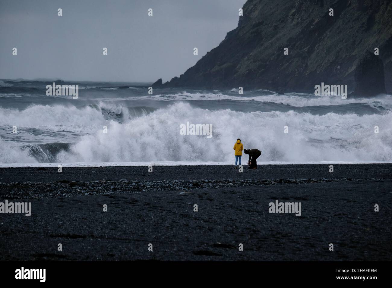 I turisti che guardano il surf sulla spiaggia Nera nell'Islanda meridionale in una fredda giornata trascorsa Foto Stock