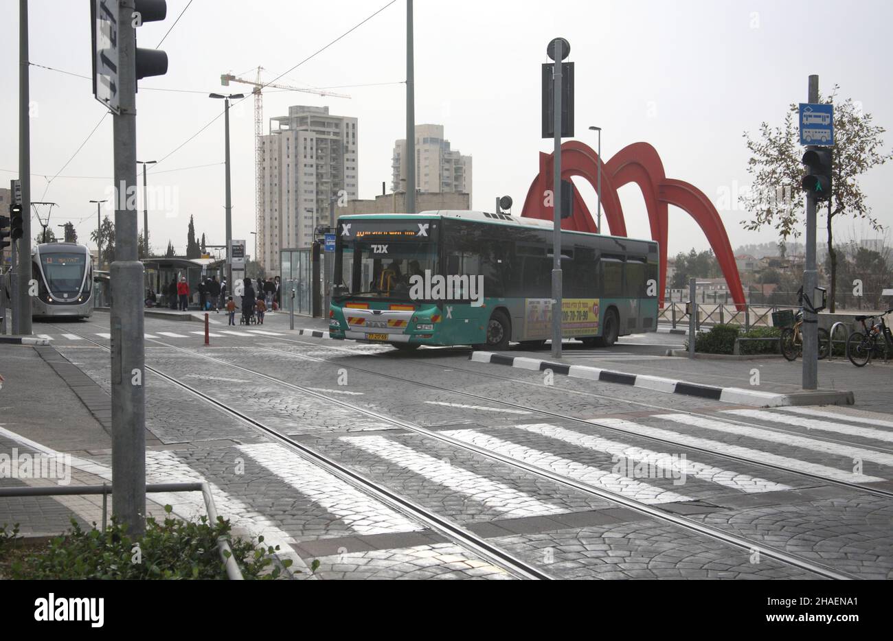 L'autobus attraversa l'incrocio mentre la Light Rail attende alla stazione di Mount Herzl, sulla destra è l'omaggio di Alexander Calder alla scultura di Gerusalemme. Foto Stock