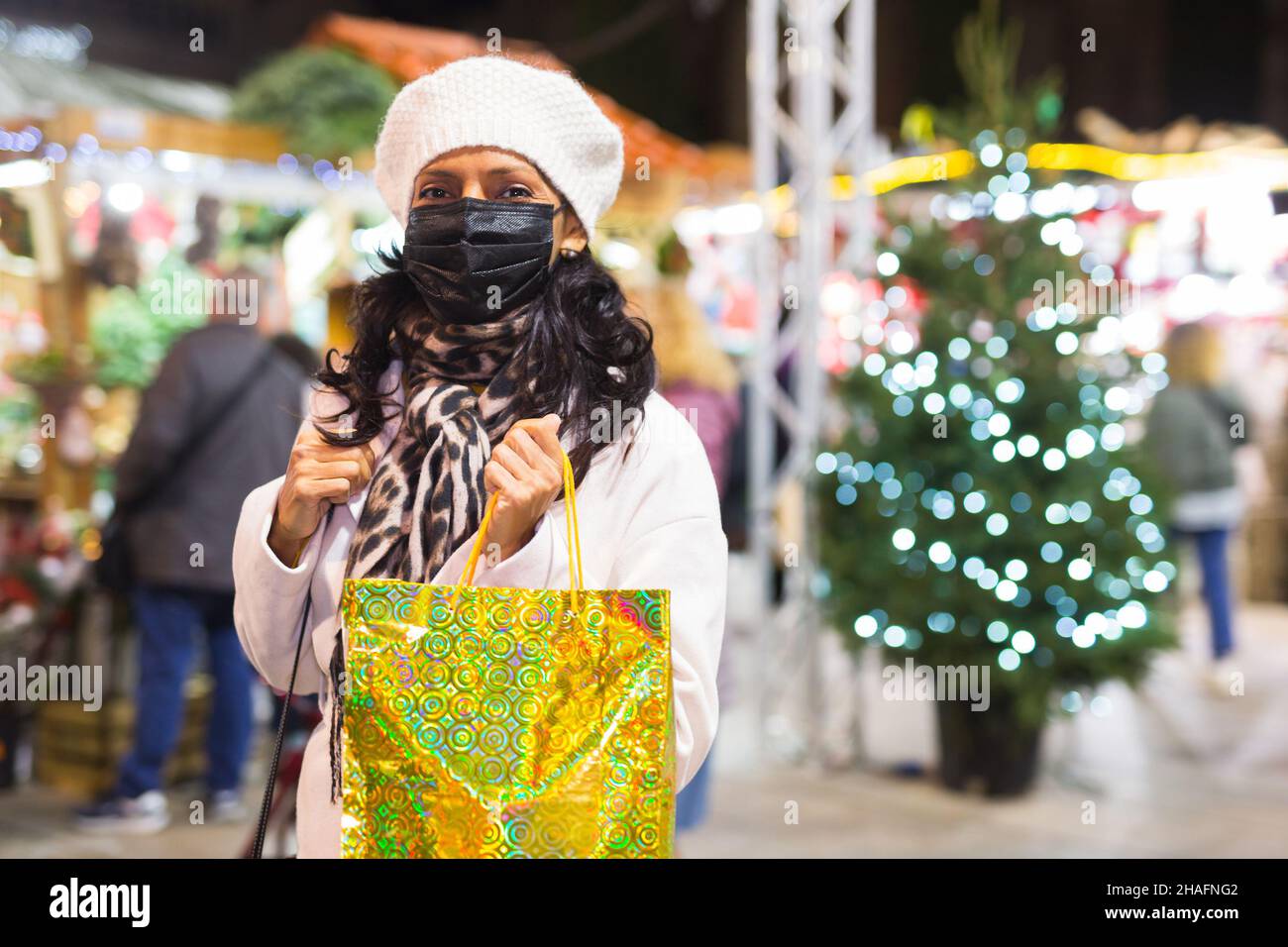 Donna in maschera protettiva con sacchetti di carta shopping alla fiera di Natale Foto Stock