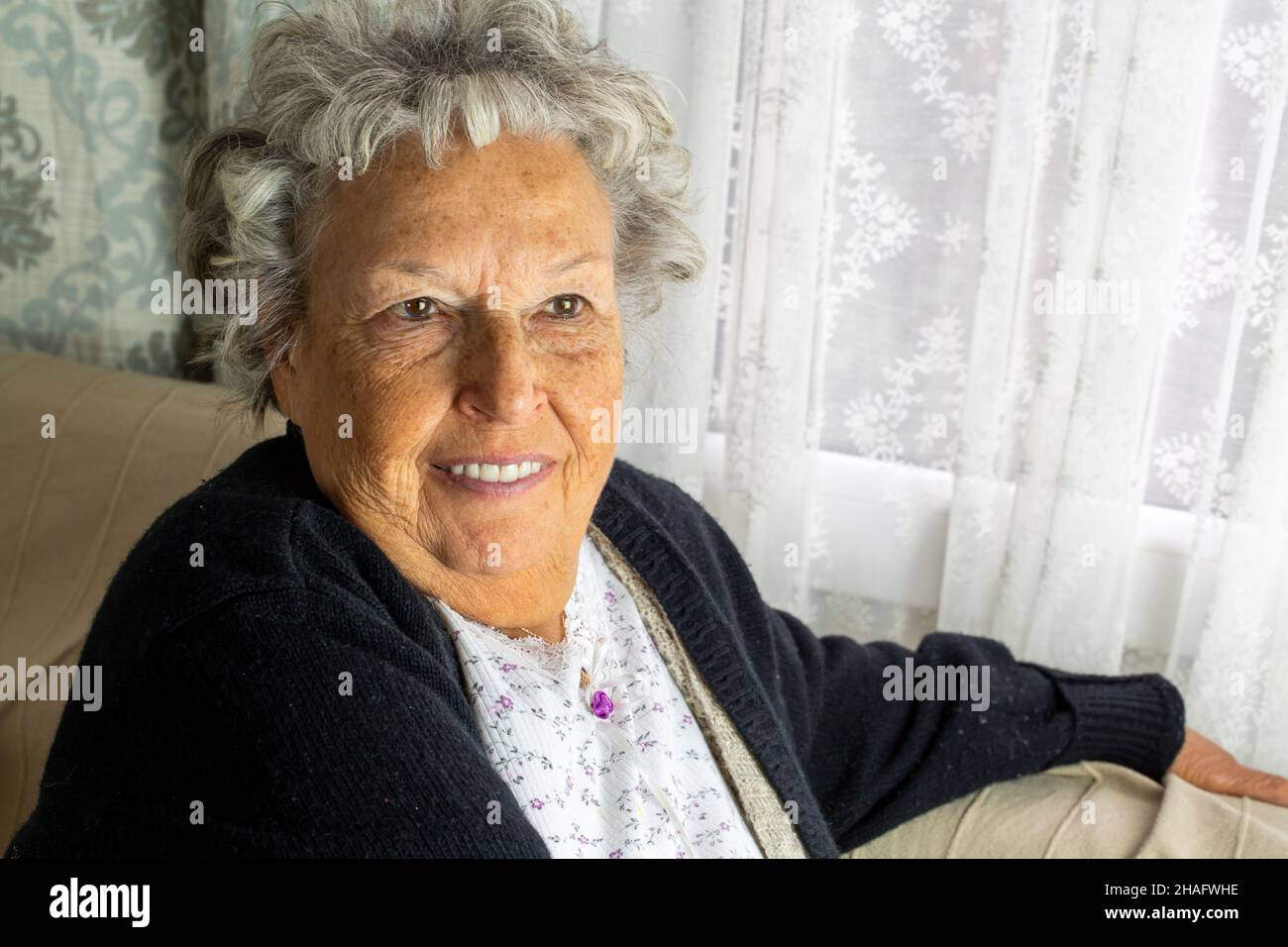 Ritratto di donna anziana sorridente, seduta a casa Foto Stock