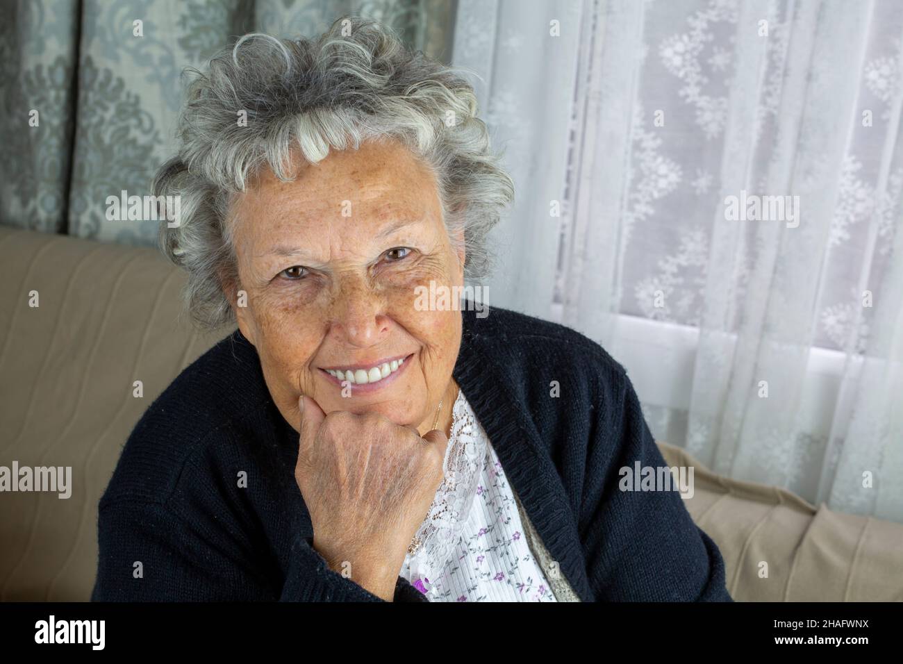 Ritratto di donna anziana sorridente, seduta a casa Foto Stock