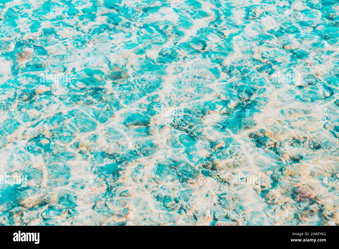 Superficie d'acqua bianca e blu vibrante con onde trasparenti chiare e un bel sole che risplende sulle barriere coralline al Mar Rosso o all'oceano. Sfondo concettuale astratto della texture. Concetto estivo di viaggio o vacanza Foto Stock