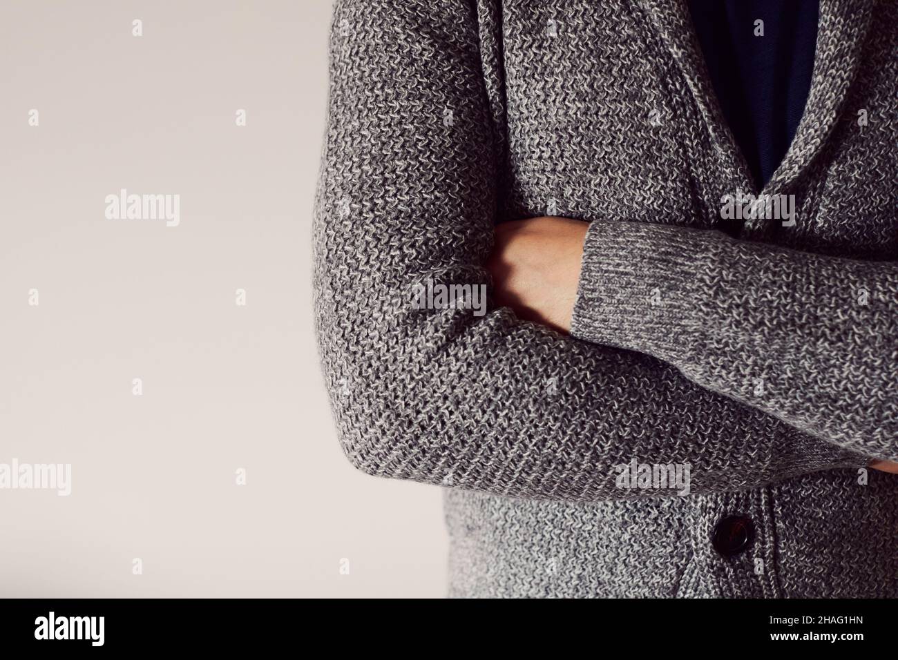 Un uomo a braccia incrociate in un cardigan su sfondo chiaro. Vista frontale. Spazio di copia. Foto Stock