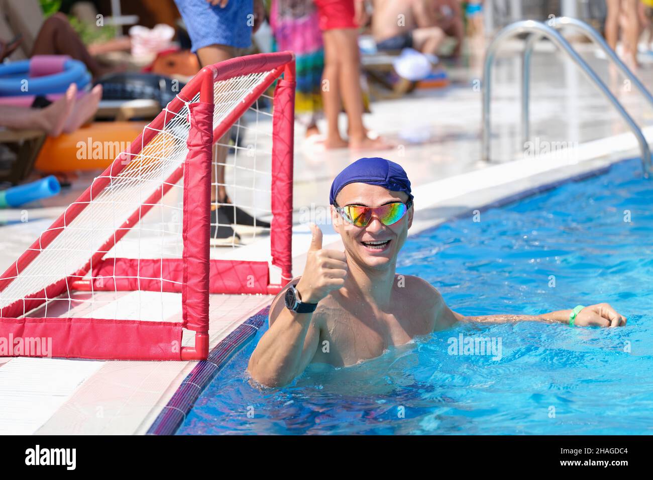 L'uomo sportivo in piscina sorride e mostra i pollici in alto Foto Stock