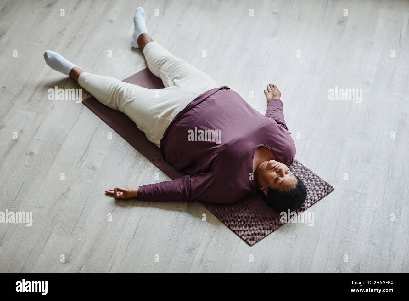 Ritratto della vista dall'alto della donna anziana nera che si trova sul pavimento con gli occhi chiusi mentre si gode l'esercizio di rilassamento Foto Stock