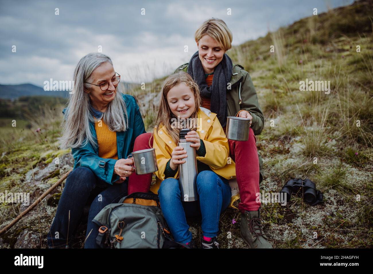 Bambina con madre e nonna seduta e bere tè caldo in cima alla montagna. Foto Stock