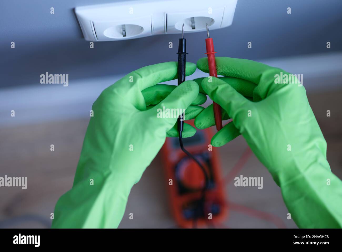 Le mani con i guanti tengono un multimetro digitale vicino alla presa Foto Stock