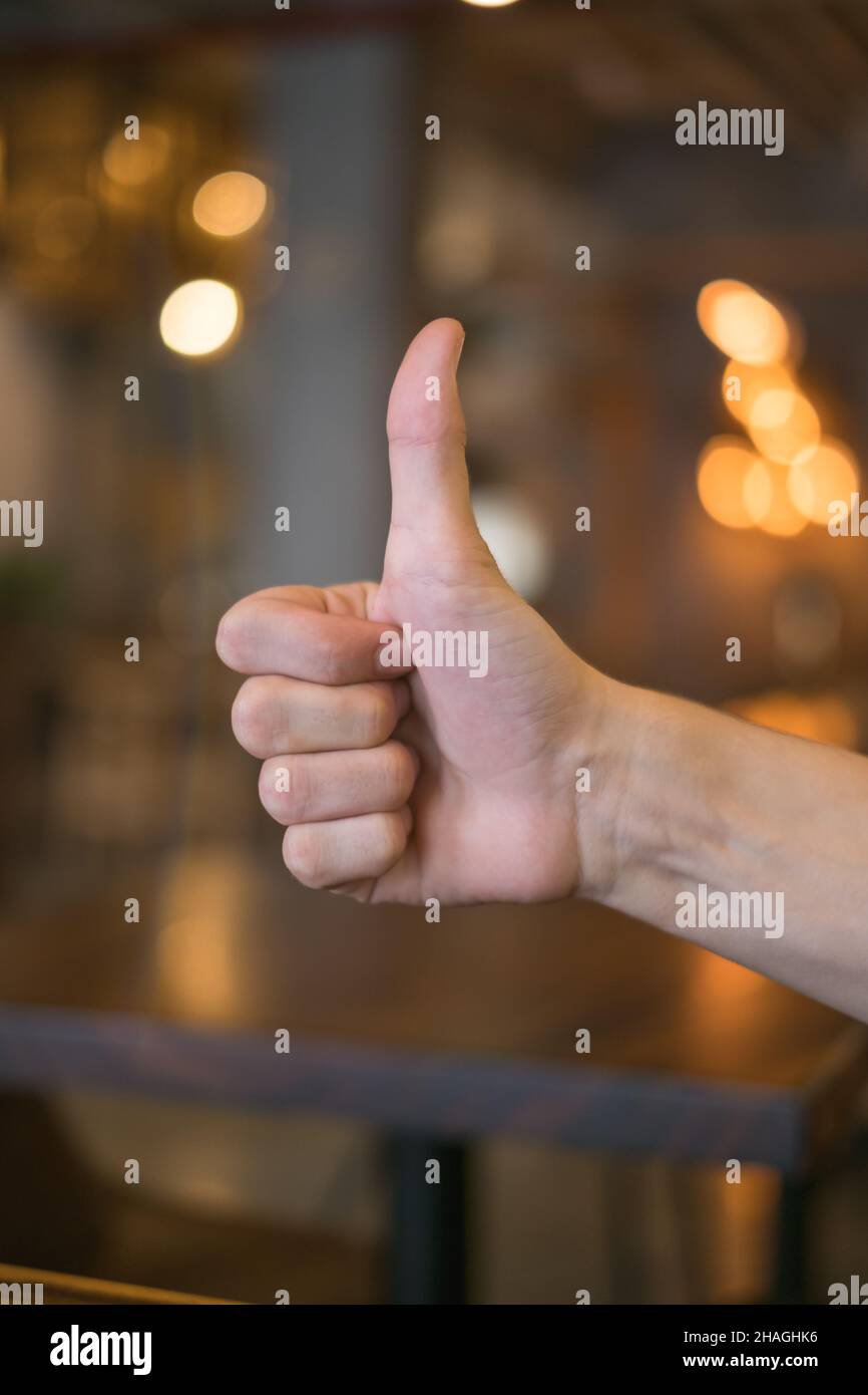 mano che mostra i pollici in su segno contro gli sfondi marroni con le luci in coffee shop. Foto di alta qualità Foto Stock