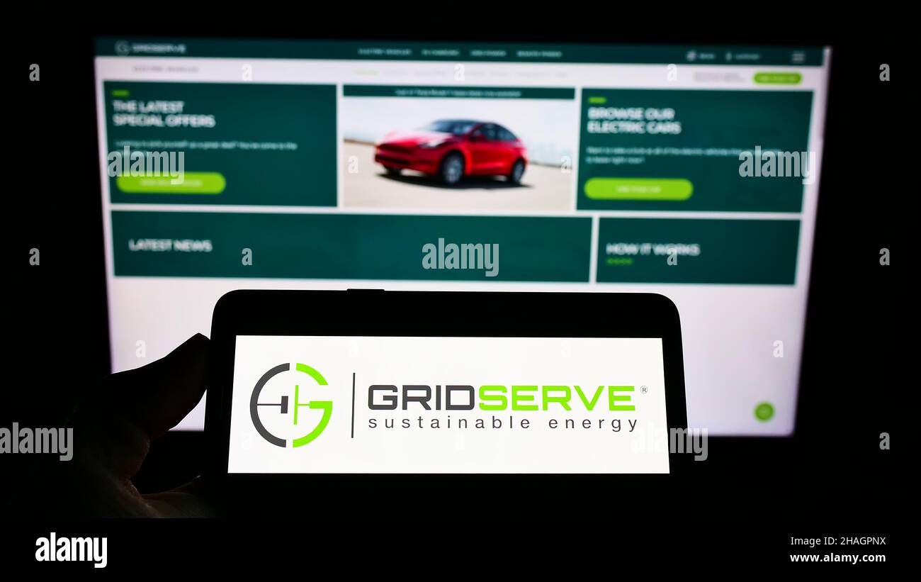 Persona che detiene il telefono cellulare con il logo della società britannica GRIDSERVE Sustainable Energy Ltd sullo schermo di fronte alla pagina web. Mettere a fuoco sul display del telefono. Foto Stock