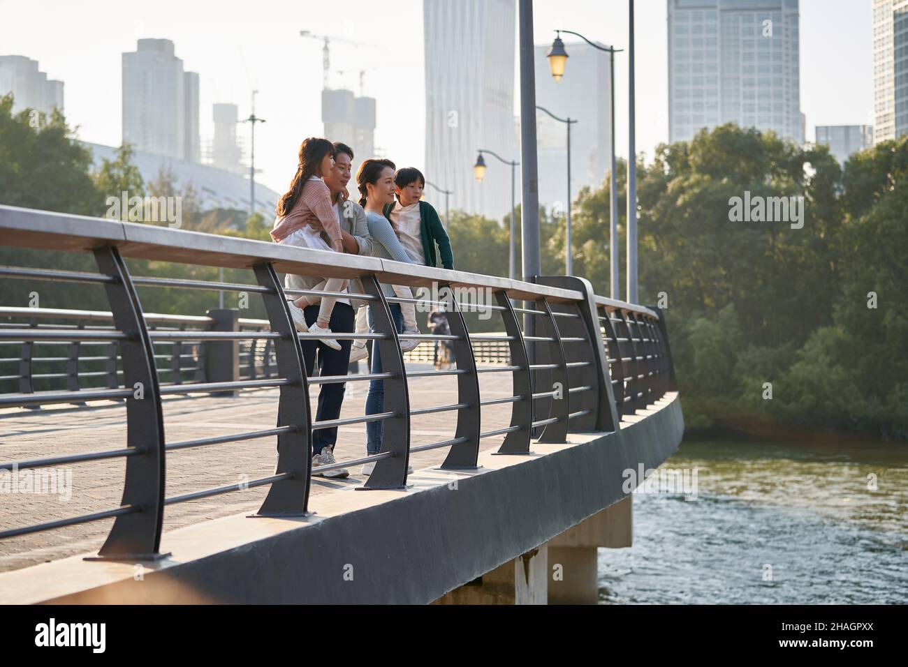 famiglia asiatica con due bambini in piedi su un ponte pedonale che guarda la vista del parco cittadino Foto Stock