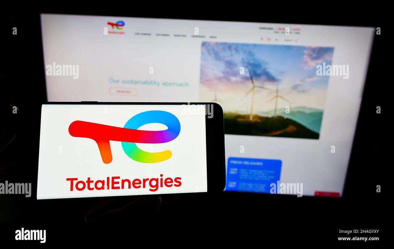 Persona che tiene smartphone con il logo della società francese TotalEnergies se di petrolio e gas sullo schermo di fronte al sito web. Mettere a fuoco sul display del telefono. Foto Stock