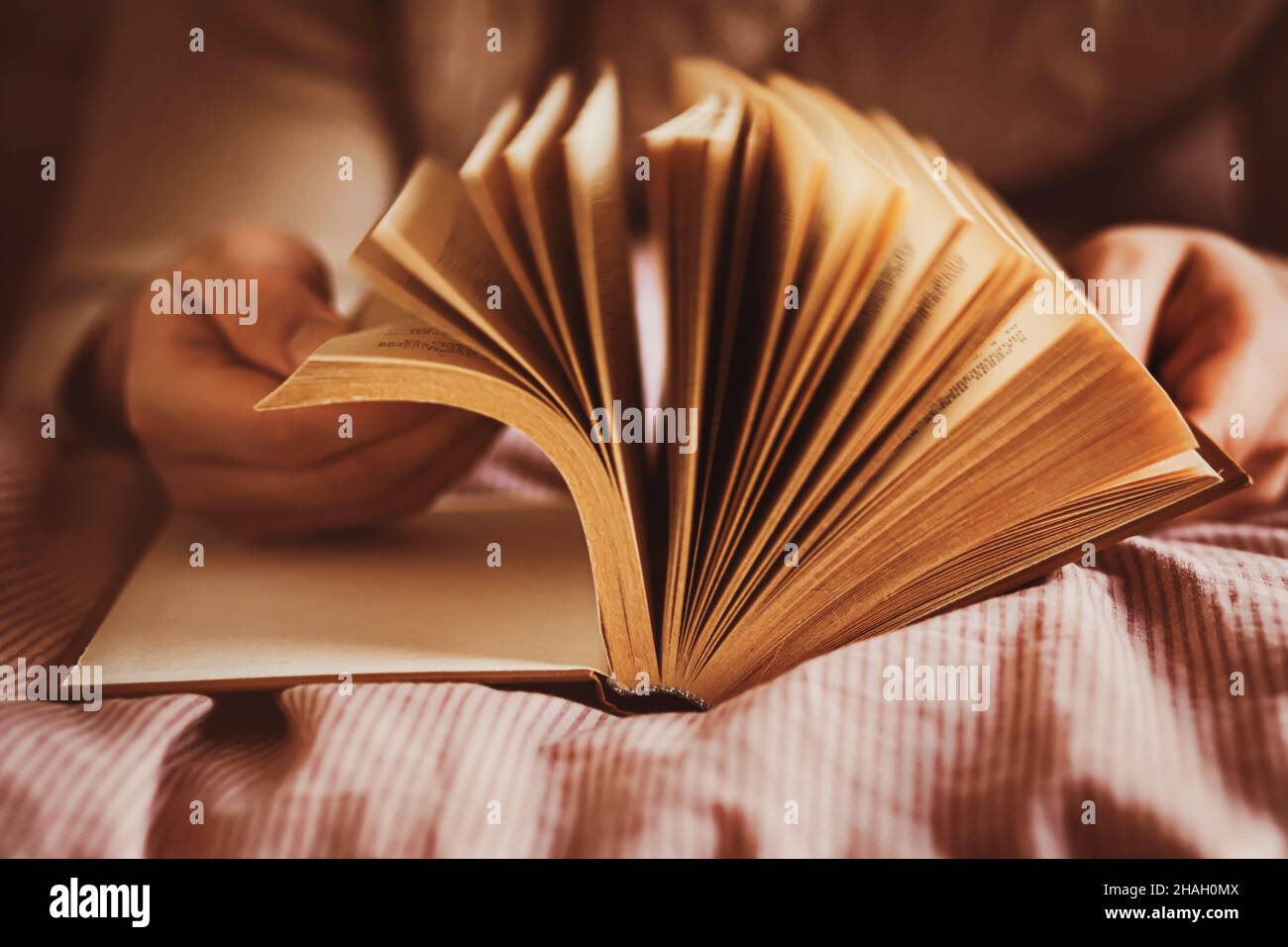 Un uomo, sdraiato su un letto morbido, si ribalta attraverso le vecchie pagine di un folto libro interessante. Autosviluppo a casa. Tempo libero e ricreazione durante la lettura. Foto Stock