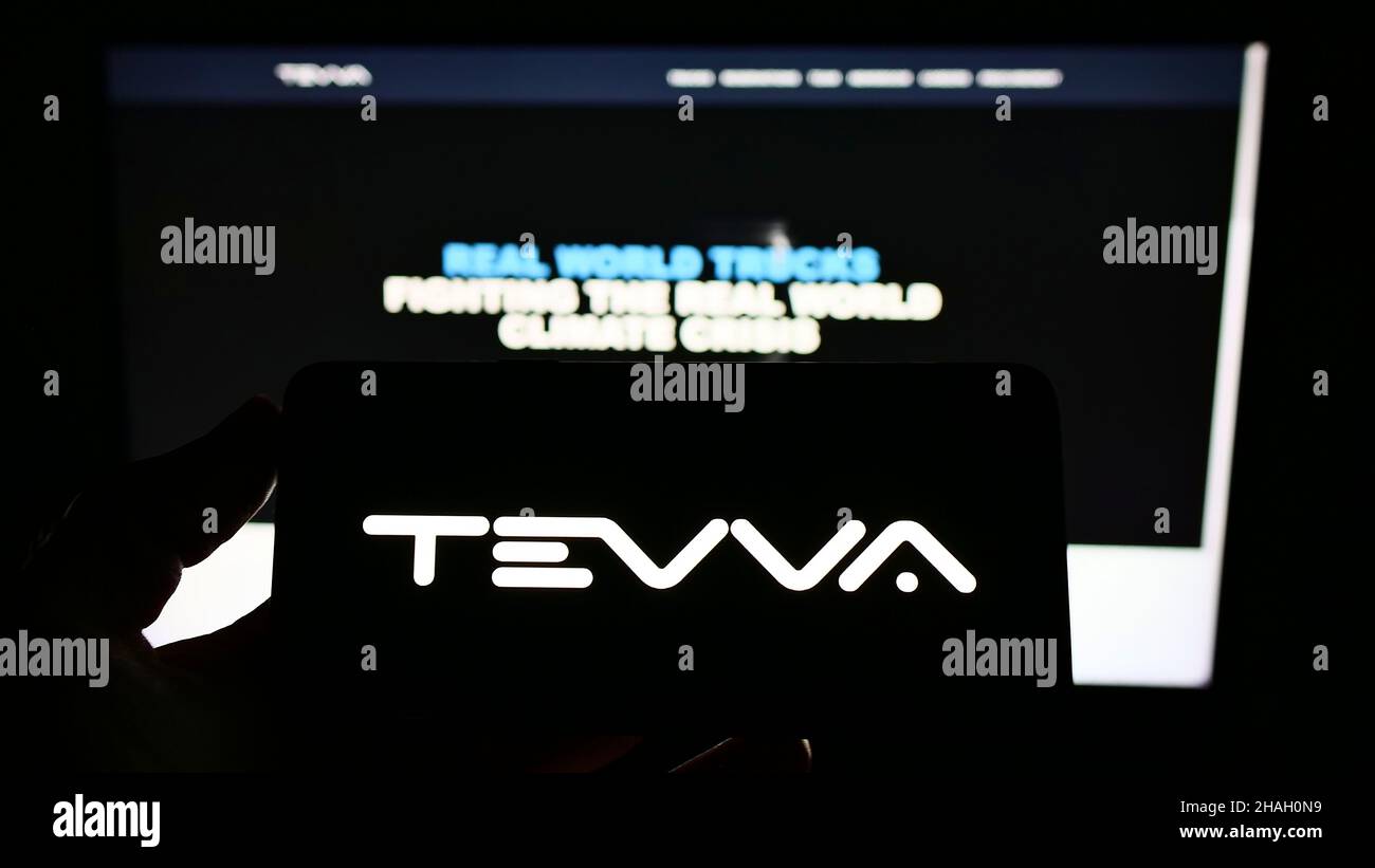 Persona che tiene uno smartphone con il logo della società britannica di camion elettrici Tevva Motors Limited sullo schermo di fronte al sito web. Mettere a fuoco sul display del telefono. Foto Stock