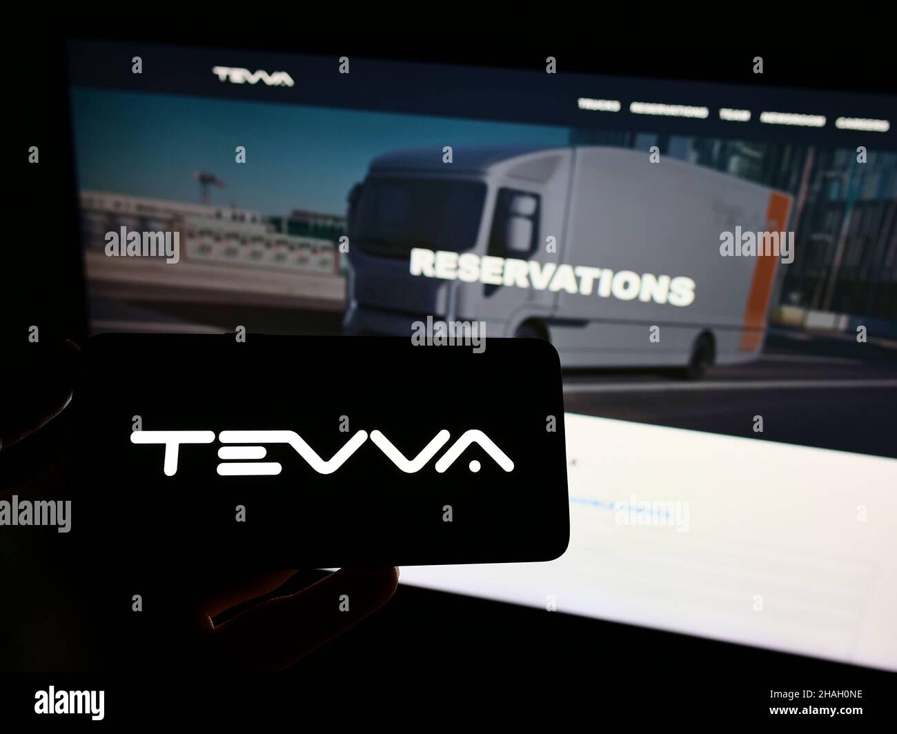 Persona che detiene il telefono cellulare con il logo della società britannica Tevva Motors Limited camion elettrici sullo schermo di fronte alla pagina web. Mettere a fuoco sul display del telefono. Foto Stock