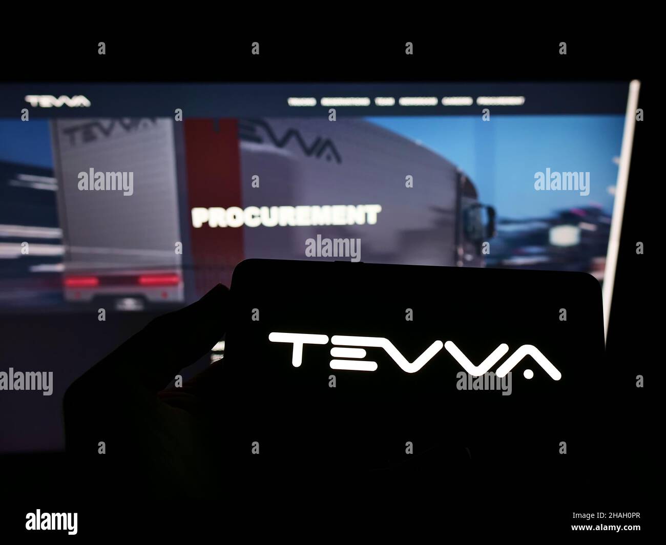 Persona che detiene il cellulare con il logo della società britannica Tevva Motors Limited camion elettrici sullo schermo di fronte al sito web. Mettere a fuoco sul display del telefono. Foto Stock