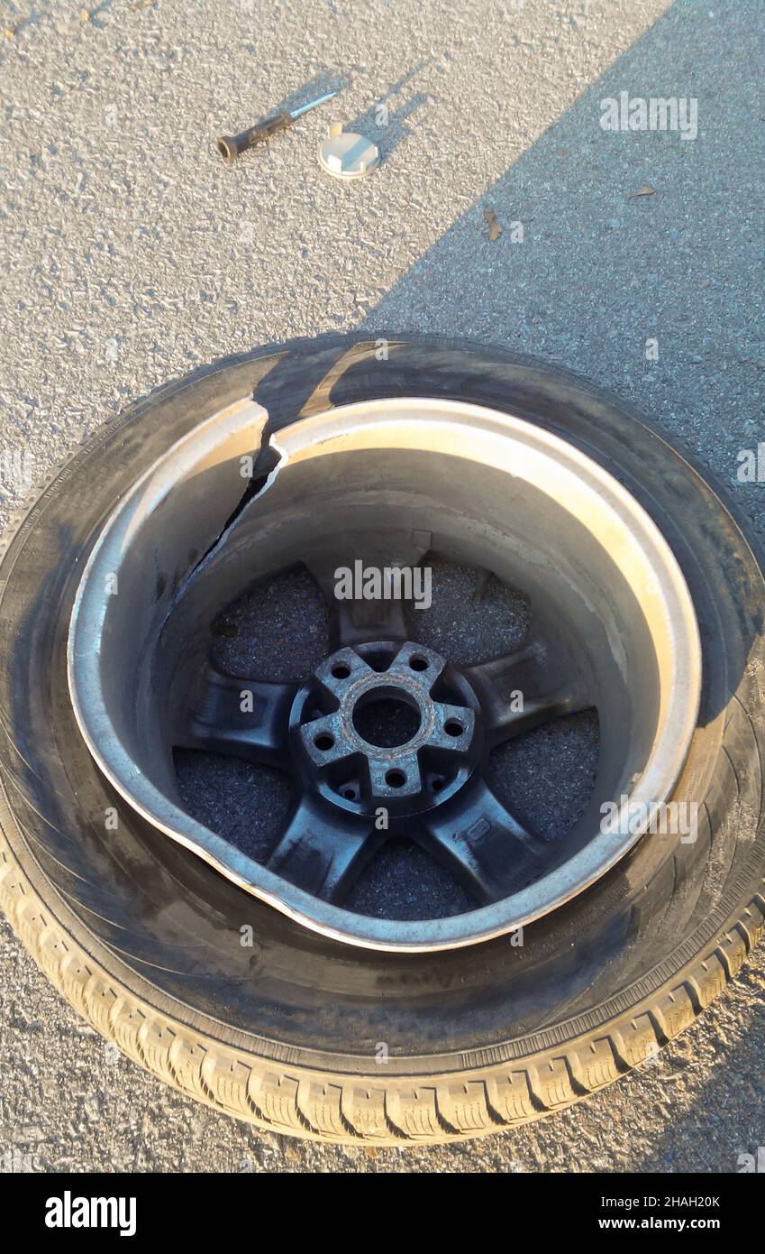 Sul primo piano dell'asfalto si trova una ruota di un'auto con una ruota in lega divisa, schiacciata in un buco sulla strada Foto Stock