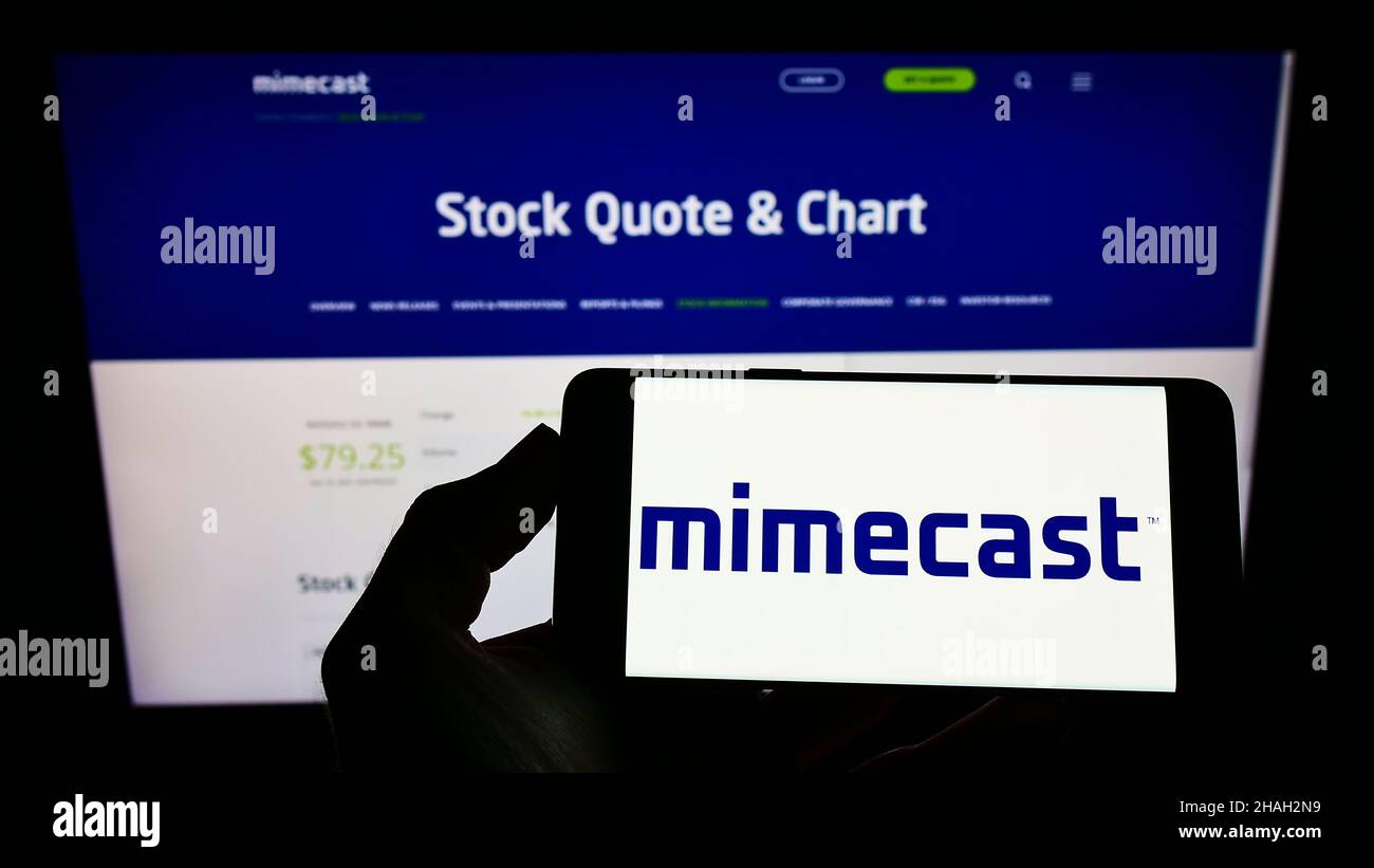 Persona che tiene il telefono cellulare con il logo della società di gestione della posta elettronica Mimecast Services Limited sullo schermo di fronte alla pagina web. Mettere a fuoco sul display del telefono. Foto Stock