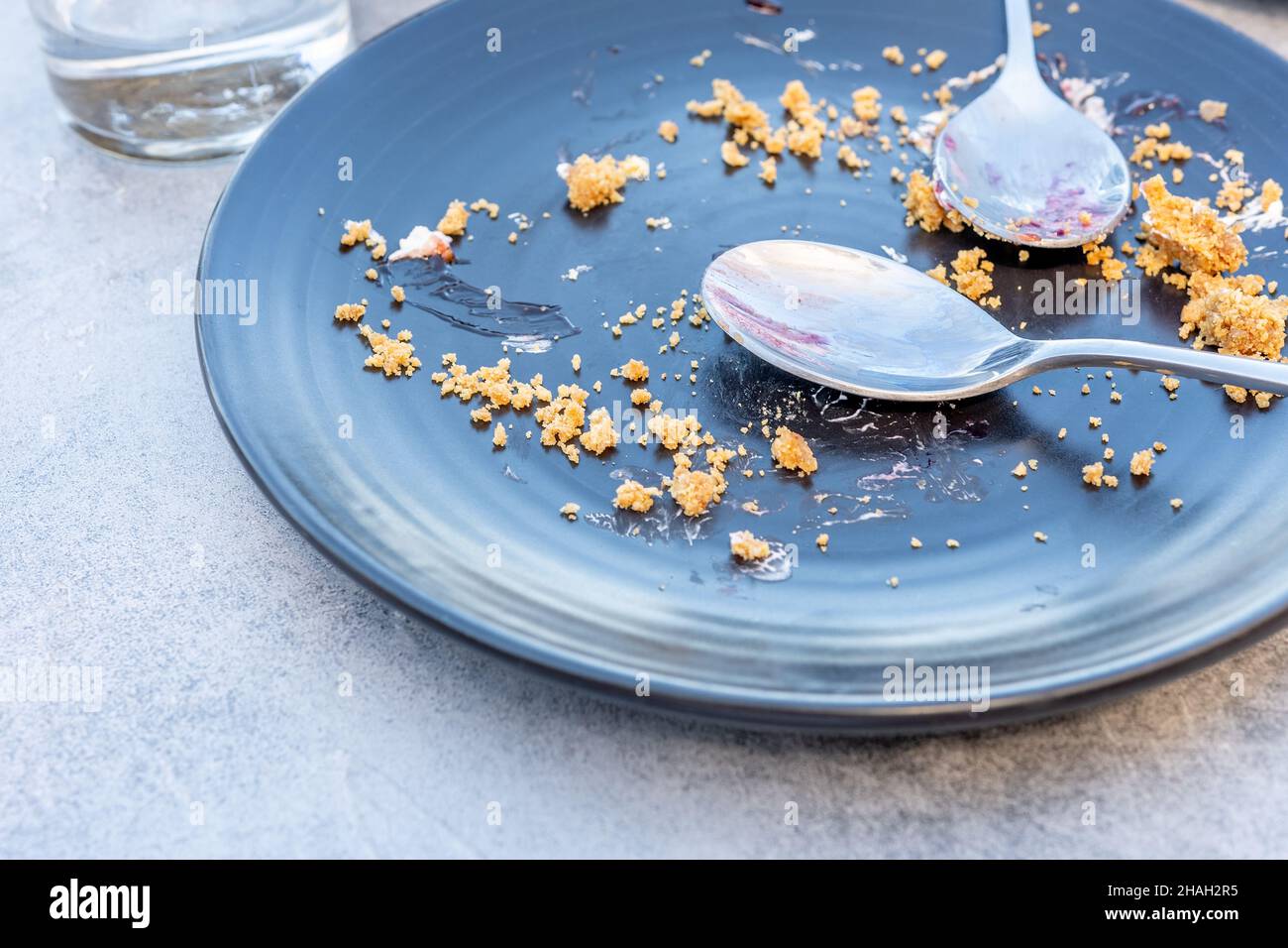 Svuotate il piatto scuro con briciole e un cucchiaio sporco su un tavolo dopo la torta dolce. Foto Stock