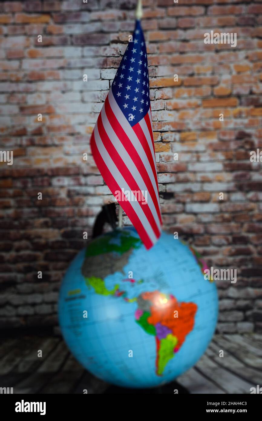 La bandiera degli Stati Uniti è contro un mondo sfocato con contorni oscuri e un muro di mattoni. Sfondo sfocato Foto Stock