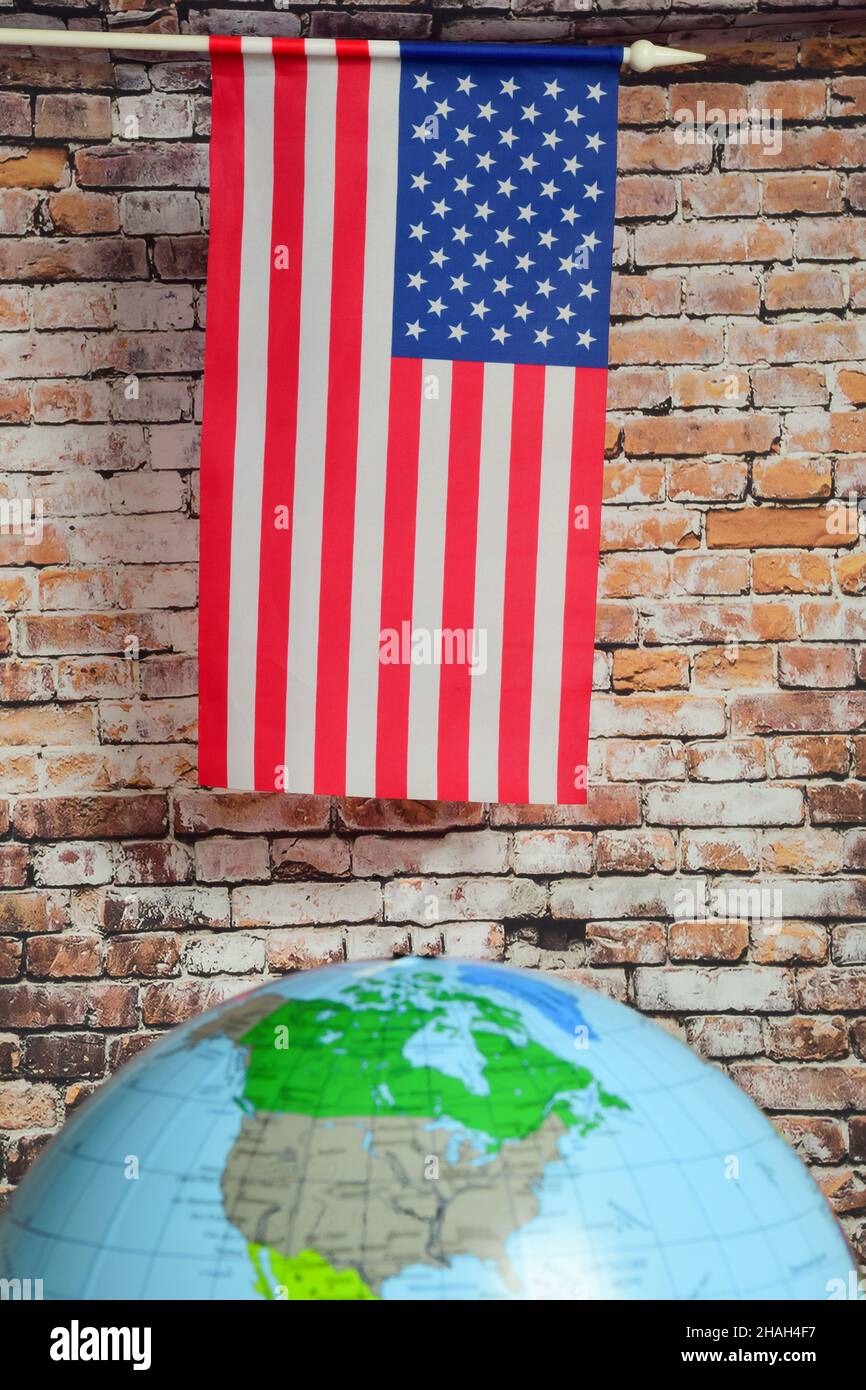 La bandiera degli Stati Uniti è posta contro un muro di mattoni marroni, al di sotto di esso si trova un globo del mondo con un indistinto contorno sfocato. Foto Stock