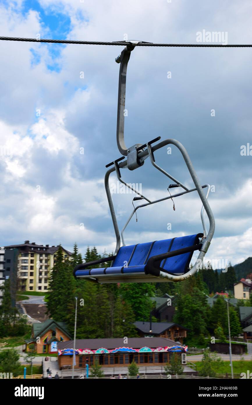 Panca ascensore vuota in movimento su una montagna in blu su uno sfondo sfocato di edifici di una località turistica estiva e cielo blu con le nuvole. Foto Stock