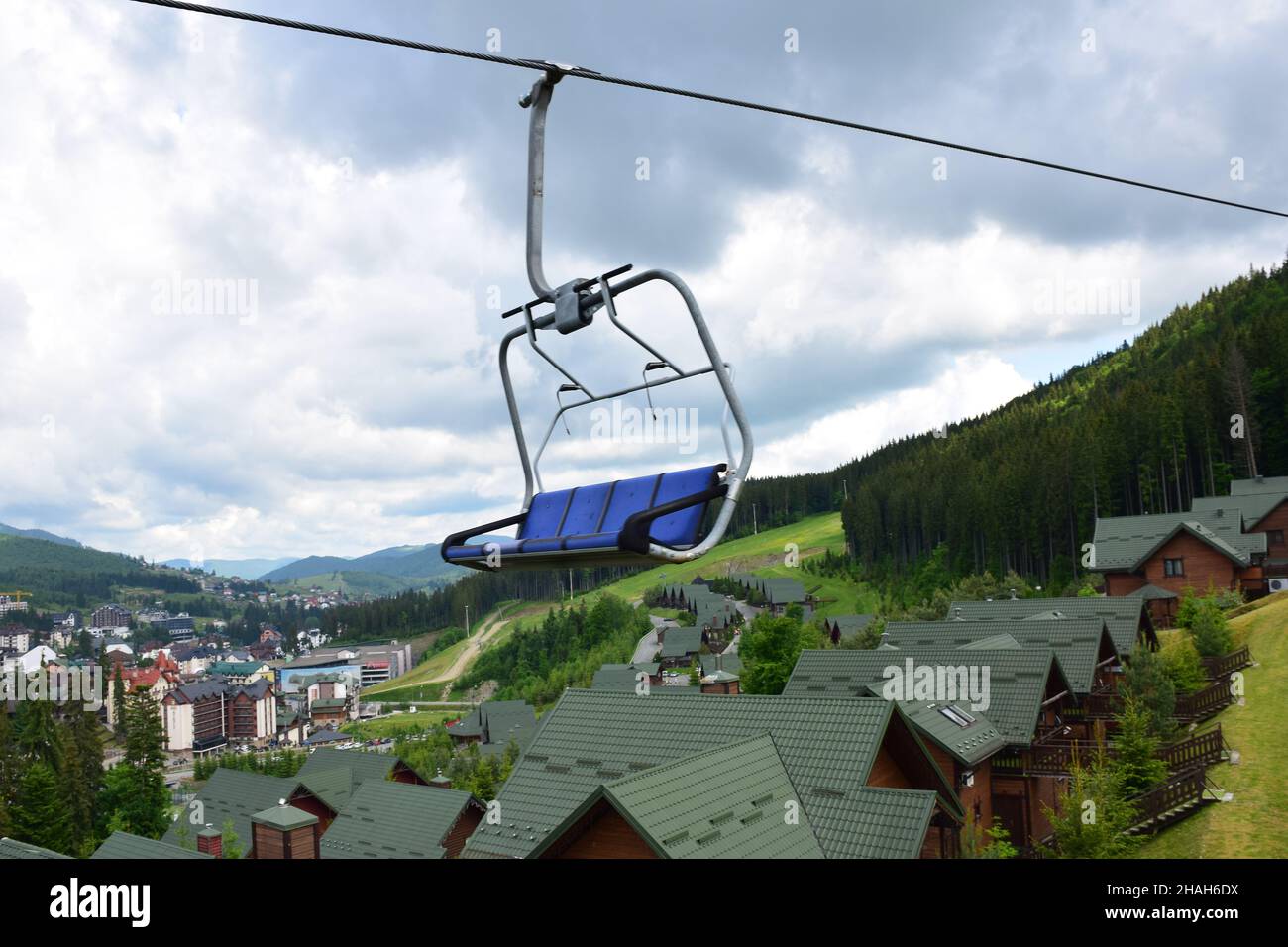 Panca ascensore vuota in movimento su una montagna in blu su uno sfondo sfocato di edifici di una località turistica estiva e cielo blu con le nuvole. Foto Stock