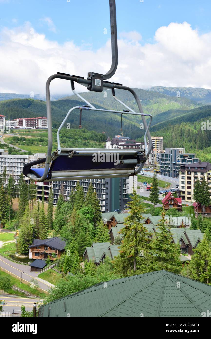 Panca ascensore vuota in movimento su una montagna in blu su uno sfondo sfocato di edifici di una località turistica estiva e cielo blu con le nuvole. Foto Stock