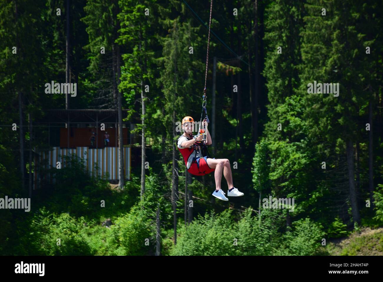 Un giovane uomo in un casco saltò dal bungee jumping e ora si appende su una corda, oscillando e filmando se stesso su una videocamera sportiva contro una ba sfocata Foto Stock