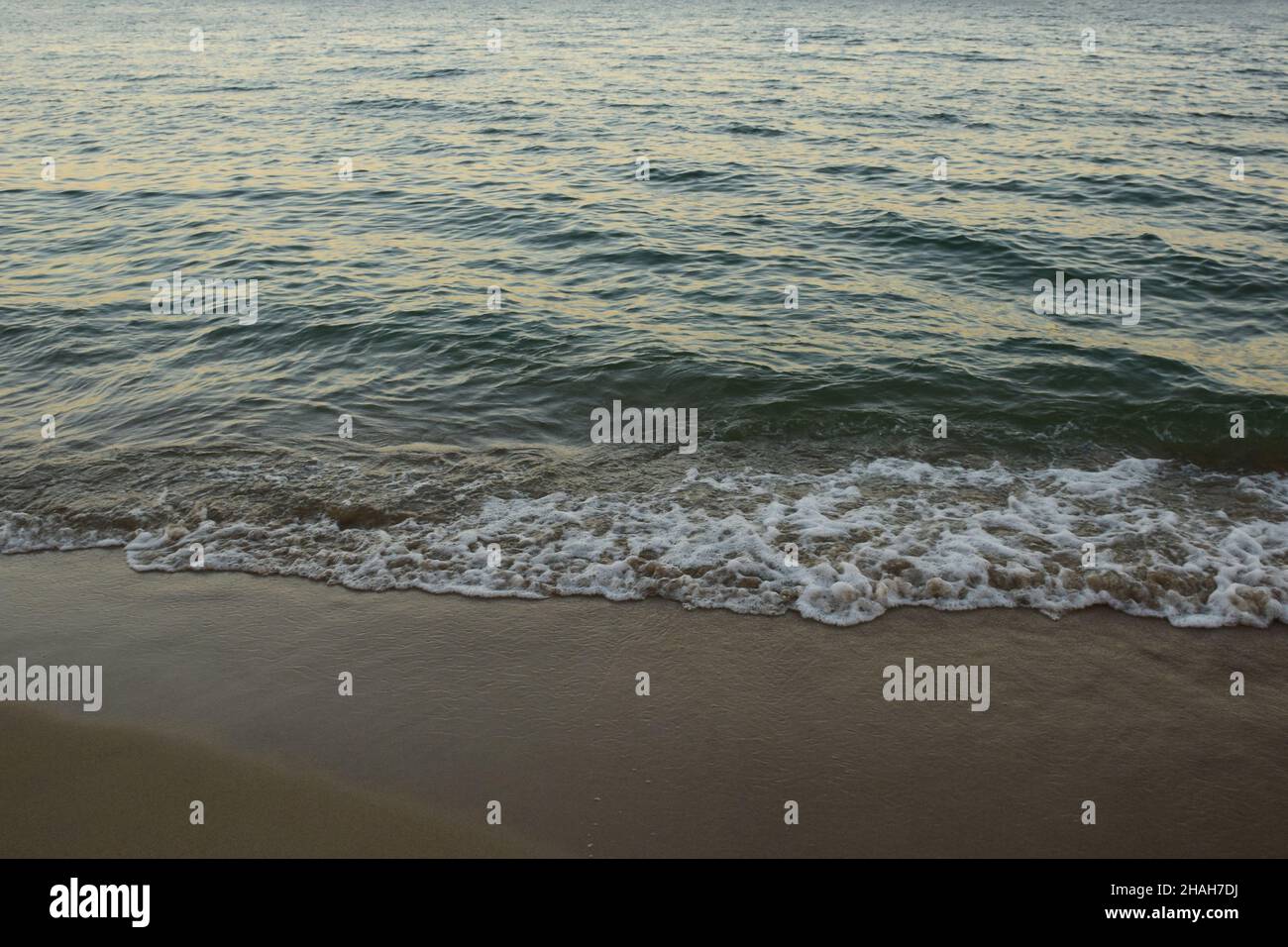 Le onde di mare schiumose rotolano sulla spiaggia di sabbia diurna Foto Stock