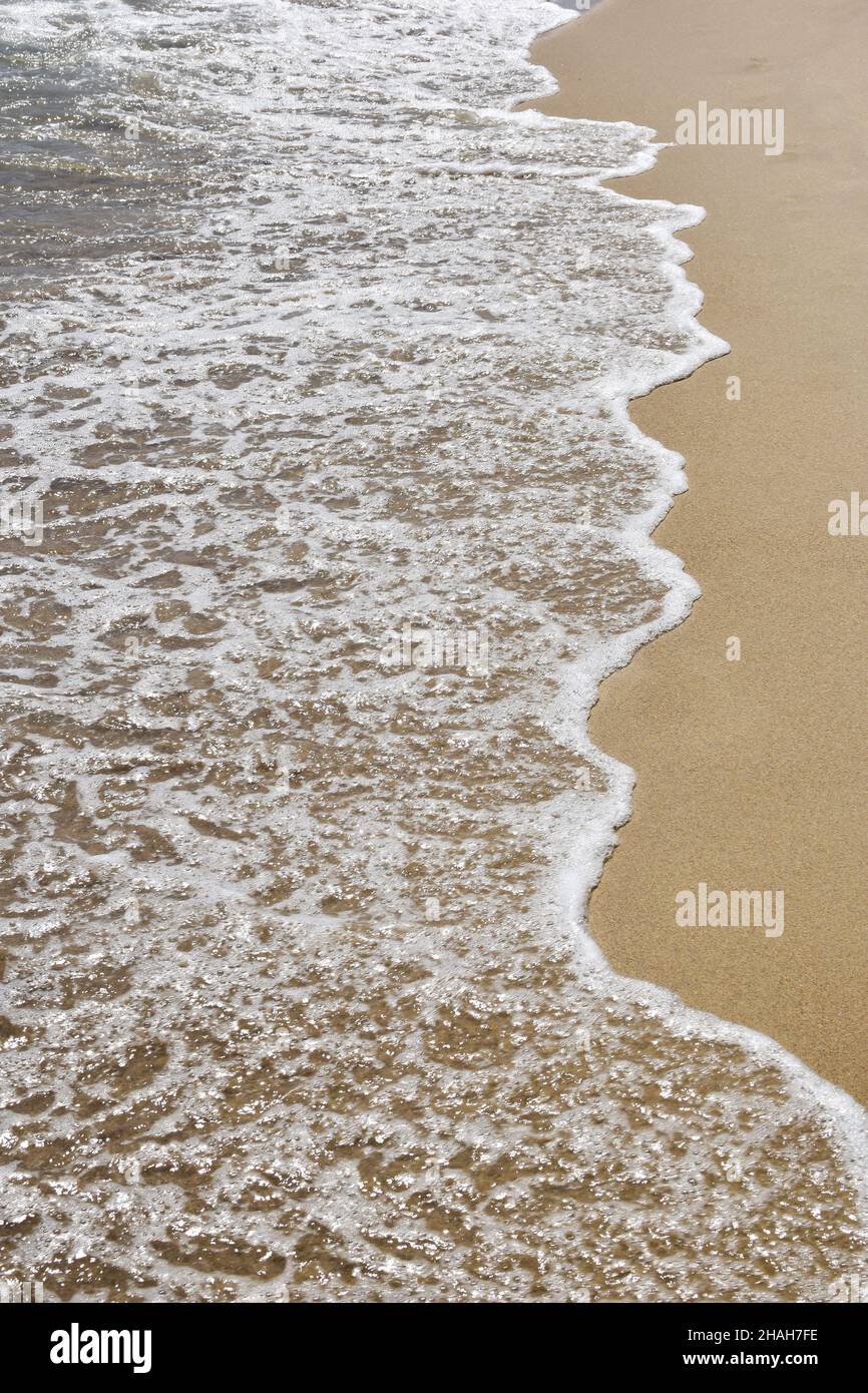 Onde di mare schiumose su una spiaggia di sabbia. Ripresa dall'alto da un'angolazione elevata Foto Stock