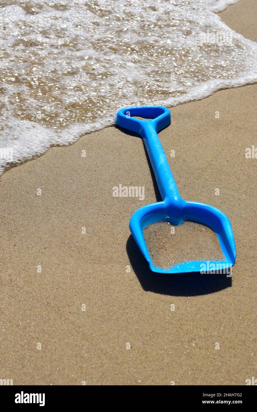 Sulla spiaggia di sabbia del mare si trova una pala del bambino sullo sfondo di un'onda schiumosa. Primo piano fotografato Foto Stock