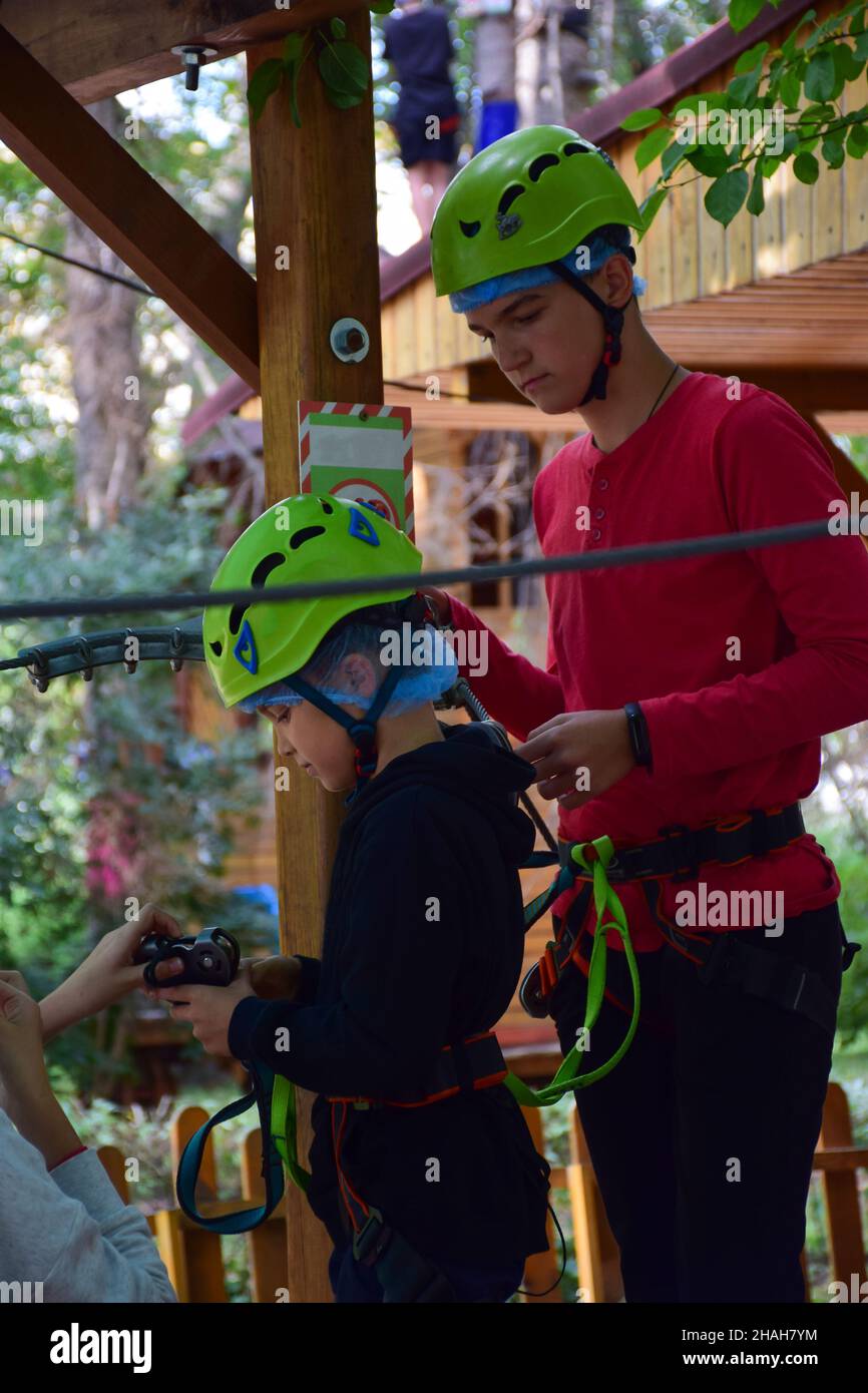 Due ragazzi di diverse età e altezze si stanno preparando su di loro un'imbracatura di sicurezza per l'arrampicata di un parco estivo in corda Foto Stock