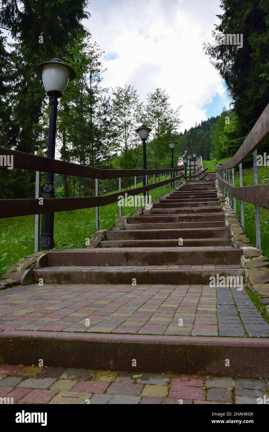 Una scalinata che conduce alla montagna con scalini fatti di piastrelle di pietra. Ai suoi lati ci sono lampioni e ringhiere. Molto verde. Ho fotografato Foto Stock