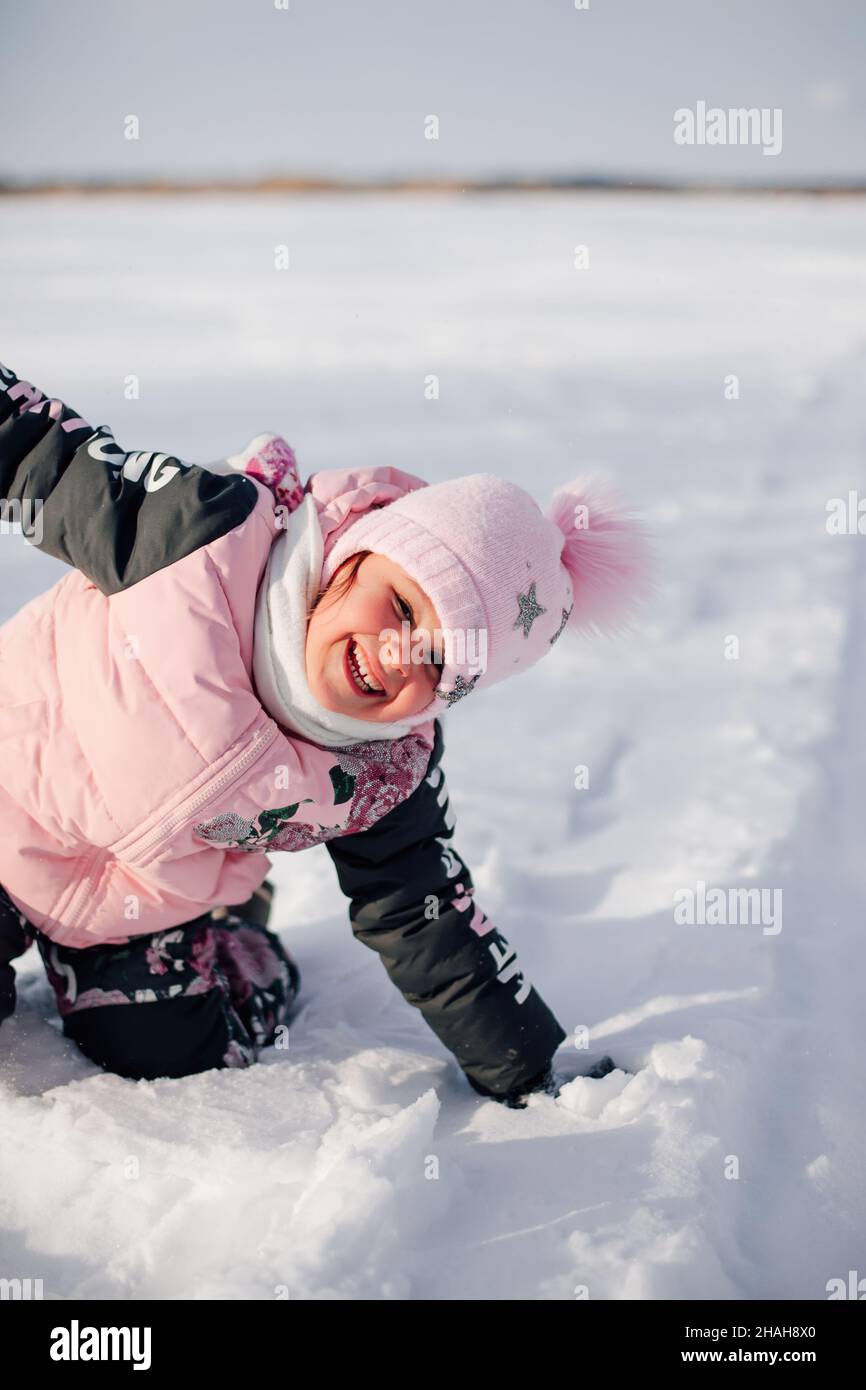 A bambini piace camminare all'aria aperta. Bambina in giacca rosa invernale e cappello con pompom divertirsi a piedi nella natura e godersi il tempo di sole Foto Stock