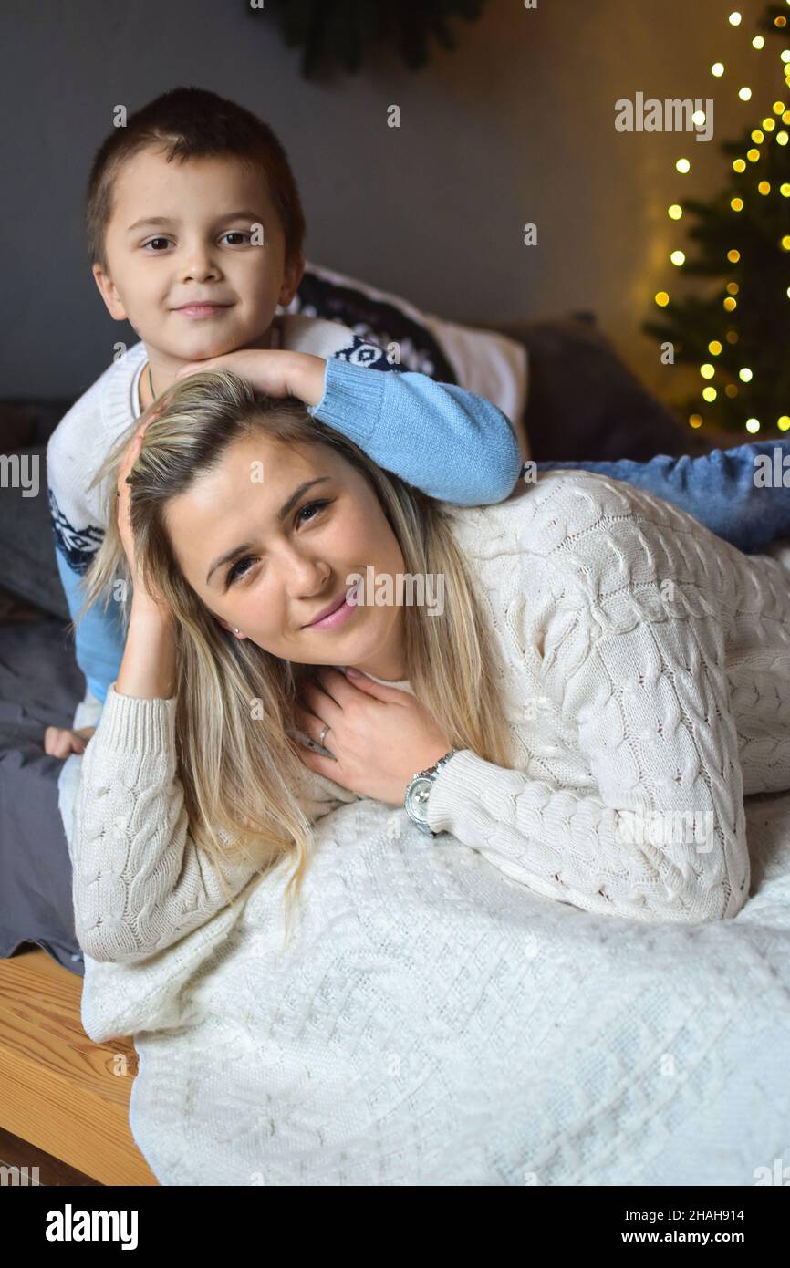 Giovane mamma bionda attraente e suo figlio stanno sorridendo e abbracciando nel soggiorno di natale. Foto Stock
