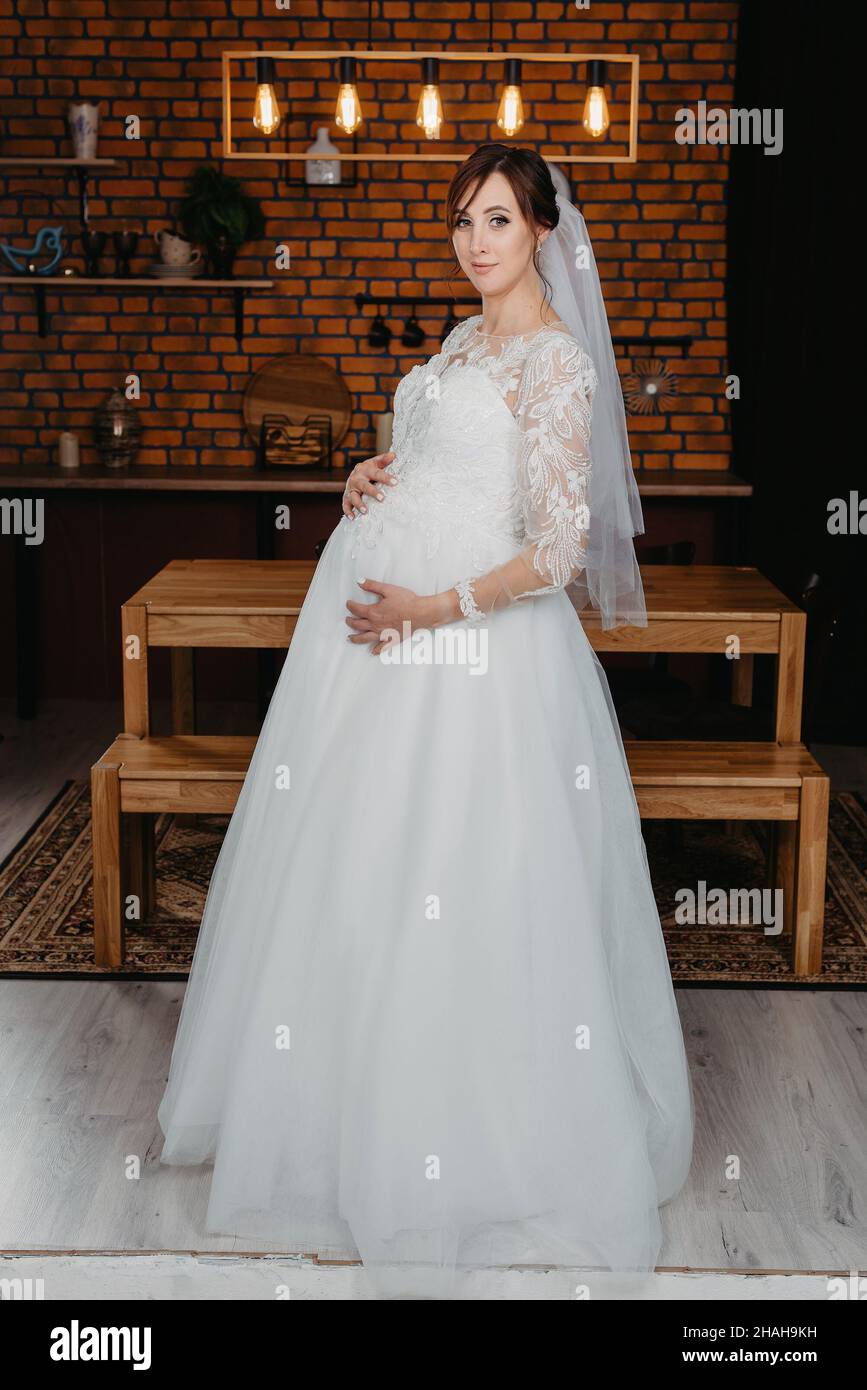 ritratto di una donna incinta in un abito da sposa bianco. donna incinta  con fiori in mano in studio Foto stock - Alamy