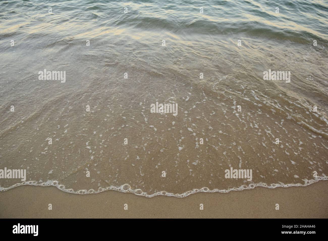 Una piccola onda di mare scorre sulla spiaggia sabbiosa con acqua trasparente e un bordo schiumoso. Fotografato dall'alto Foto Stock