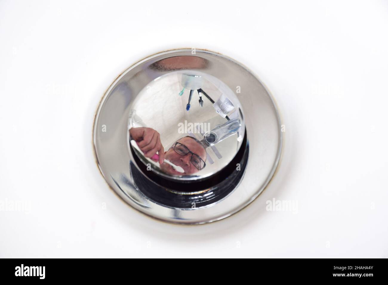 Riflesso di un uomo in bicchieri che gli spazzolano i denti nel bagno su un sughero lucido che arresta lo scarico dell'acqua. Primo piano Foto Stock