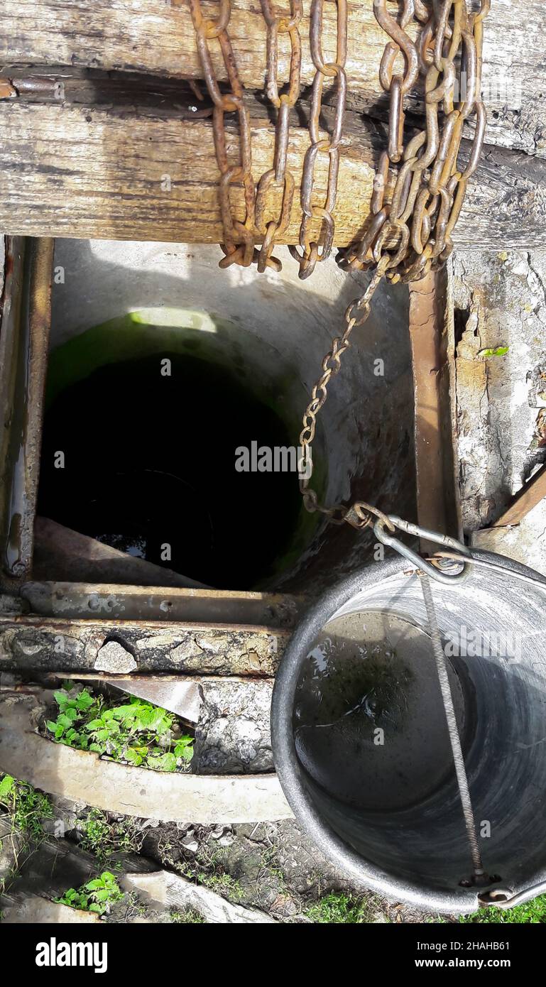 Su un vecchio pozzo, c'è un secchio di metallo legato con una catena di ferro su un foro profondo. Vista dall'alto Foto Stock