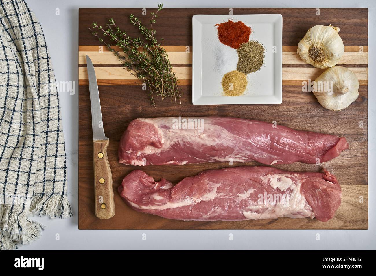 Tenderloin di maiale intero con aglio, timo e spezie su un tagliere in preparazione per la cottura Foto Stock
