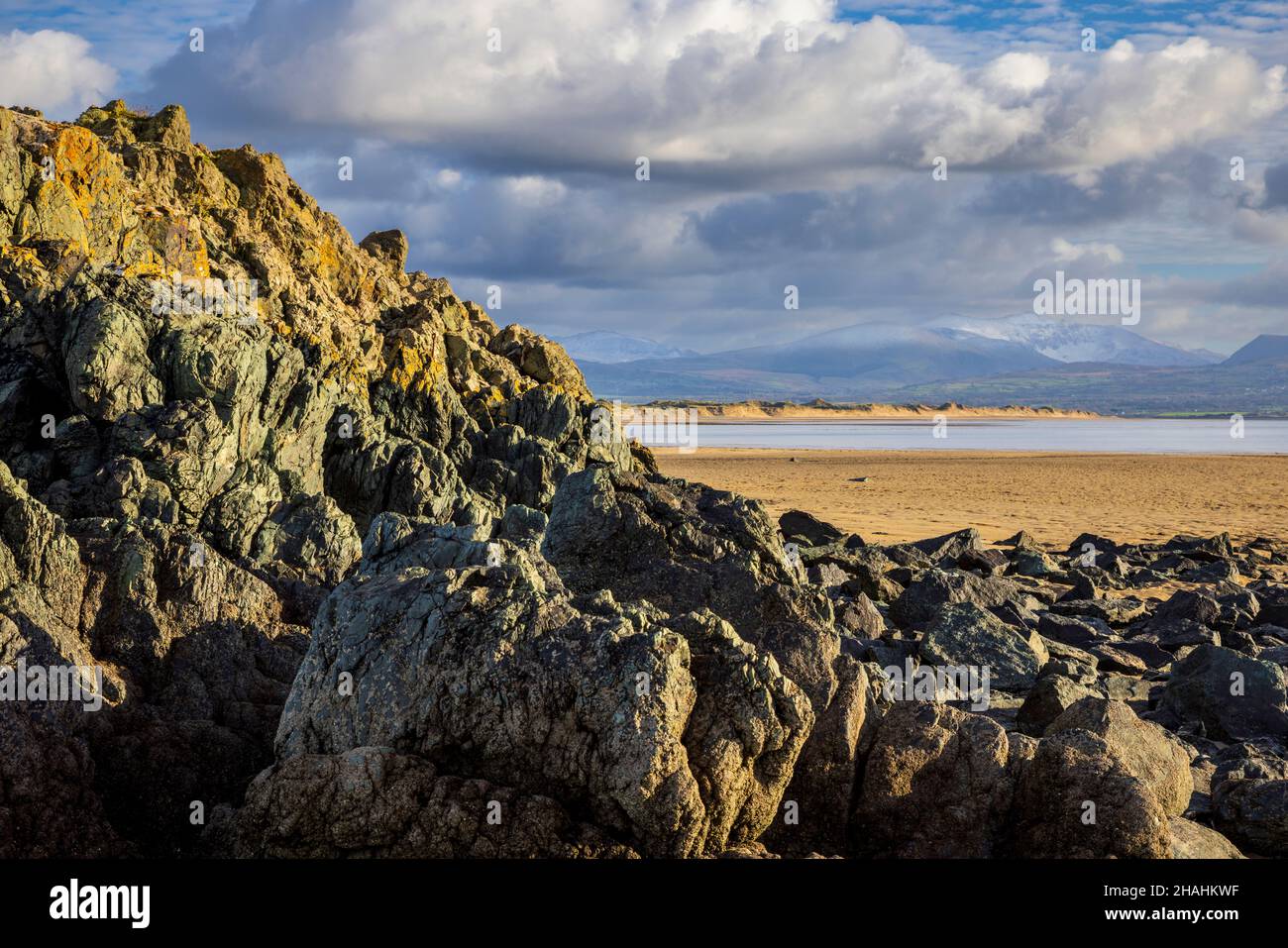 Guanciali rocce di Lava e Snowdonia Mountains da Newborough Beach, Isola di Anglesey, Galles del Nord Foto Stock