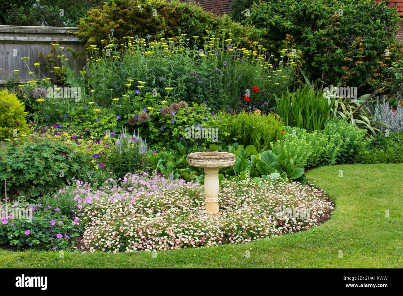 Vista di un giardino erbaceo perenne inglese bordo in estate con il bagno di uccelli come punto centrale di fuoco. Foto Stock