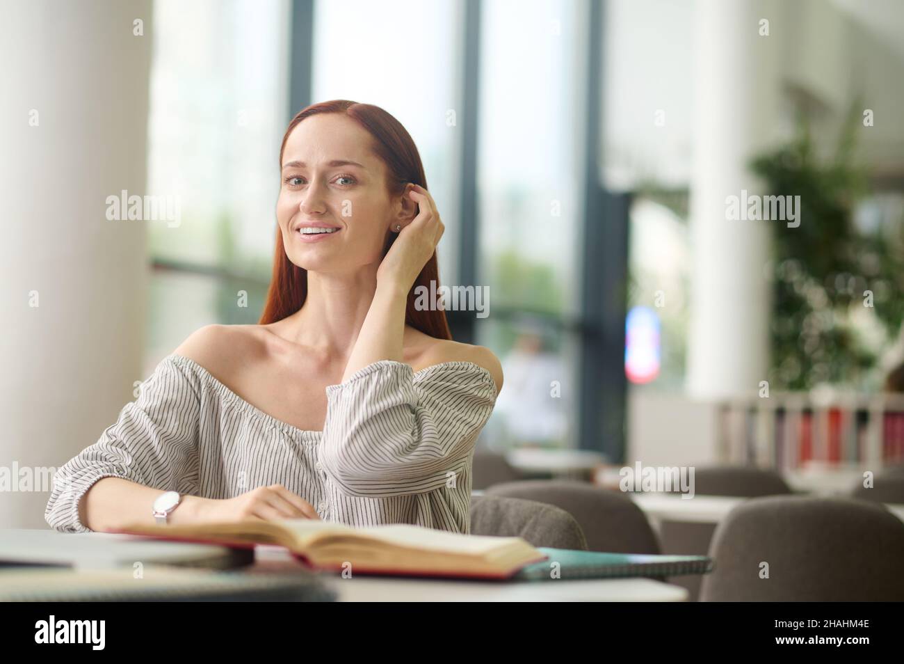 Donna con libri seduti a tavola che toccano i capelli Foto Stock