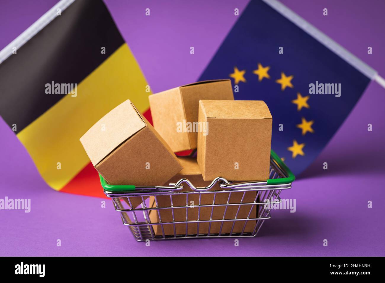 Scatole di cartone in un cestino alimentare e bandiere su sfondo colorato, concetto sul tema della distribuzione di merci belghe nell'Unione europea Foto Stock