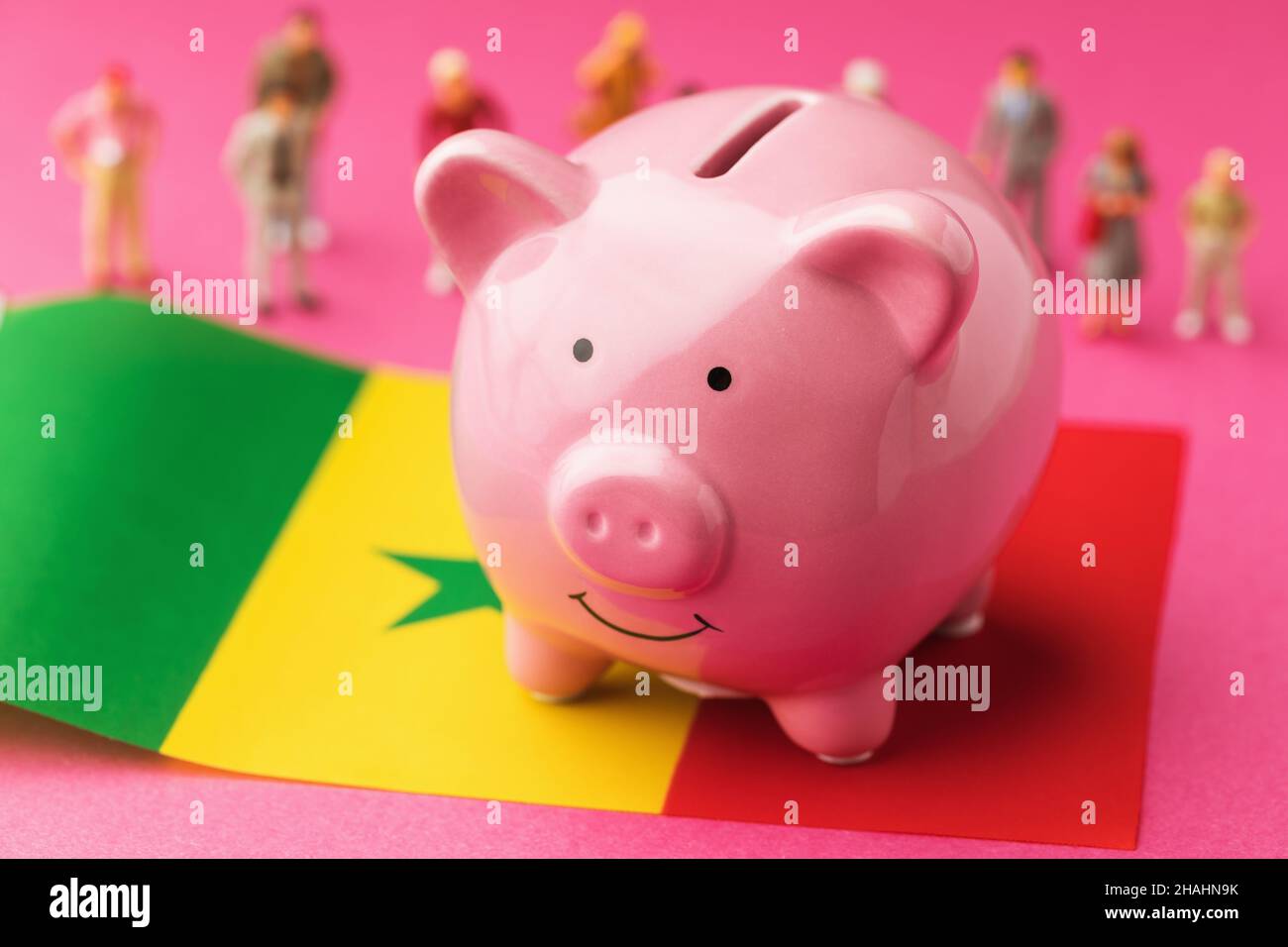 Piggy banca, bandiera senegalese e uomini giocattolo di plastica su uno sfondo colorato, concetto sul tema dei redditi della popolazione del Senegal Foto Stock