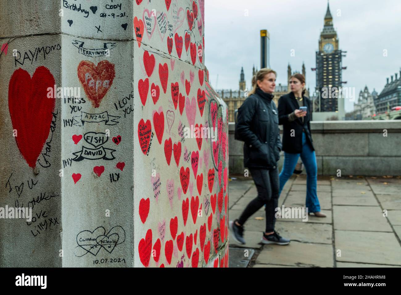 Londra, Regno Unito. 13th Dic 2021. L'arte della gente ancora sta venendo a vedere i cuori sul muro commemorativo di Covid sull'argine - dietro esso le code enormi aspettano pazientemente all'ospedale St Thomas per le vaccinazioni di richiamo di walk-in (terzo) contro Covid 19. Credit: Guy Bell/Alamy Live News Foto Stock