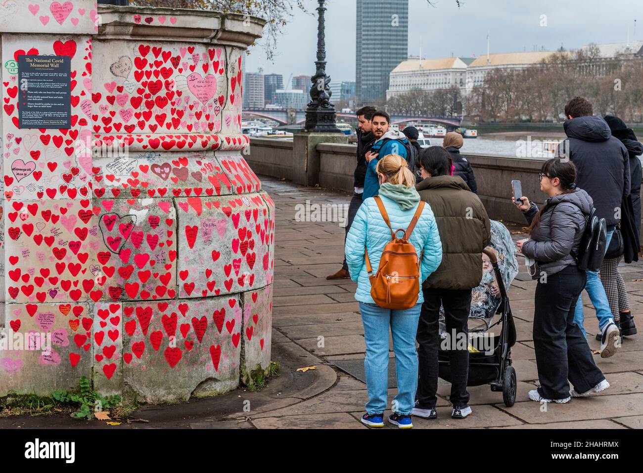 Londra, Regno Unito. 13th Dic 2021. L'arte della gente ancora sta venendo a vedere i cuori sul muro commemorativo di Covid sull'argine - dietro esso le code enormi aspettano pazientemente all'ospedale St Thomas per le vaccinazioni di richiamo di walk-in (terzo) contro Covid 19. Credit: Guy Bell/Alamy Live News Foto Stock