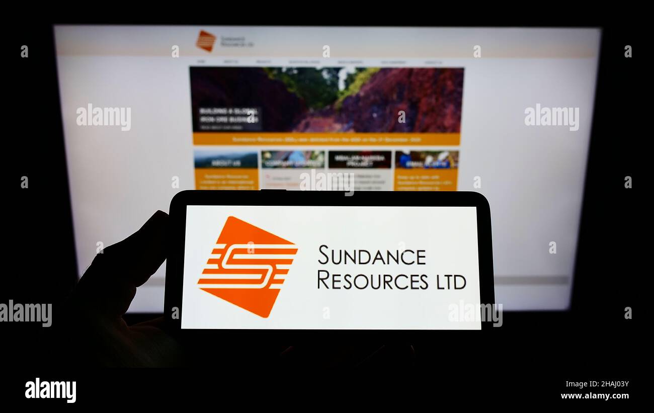 Persona che tiene smartphone con il logo della società mineraria australiana Sundance Resources Limited sullo schermo di fronte al sito web. Mettere a fuoco sul display del telefono. Foto Stock