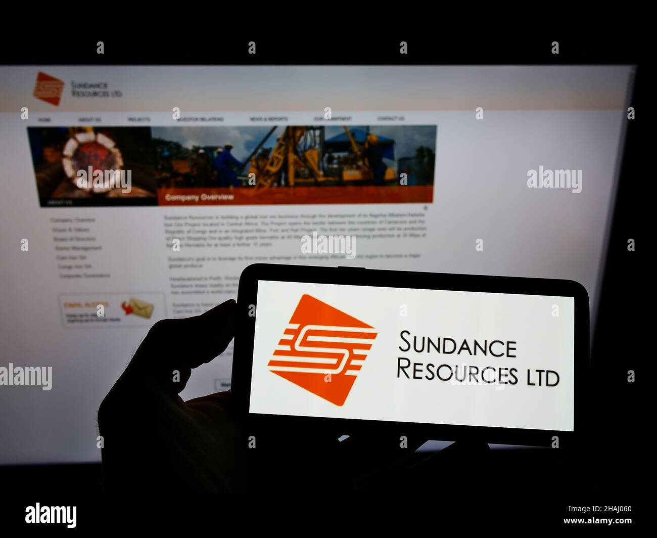 Persona che tiene il cellulare con il logo della società mineraria australiana Sundance Resources Limited sullo schermo di fronte alla pagina web. Mettere a fuoco sul display del telefono. Foto Stock