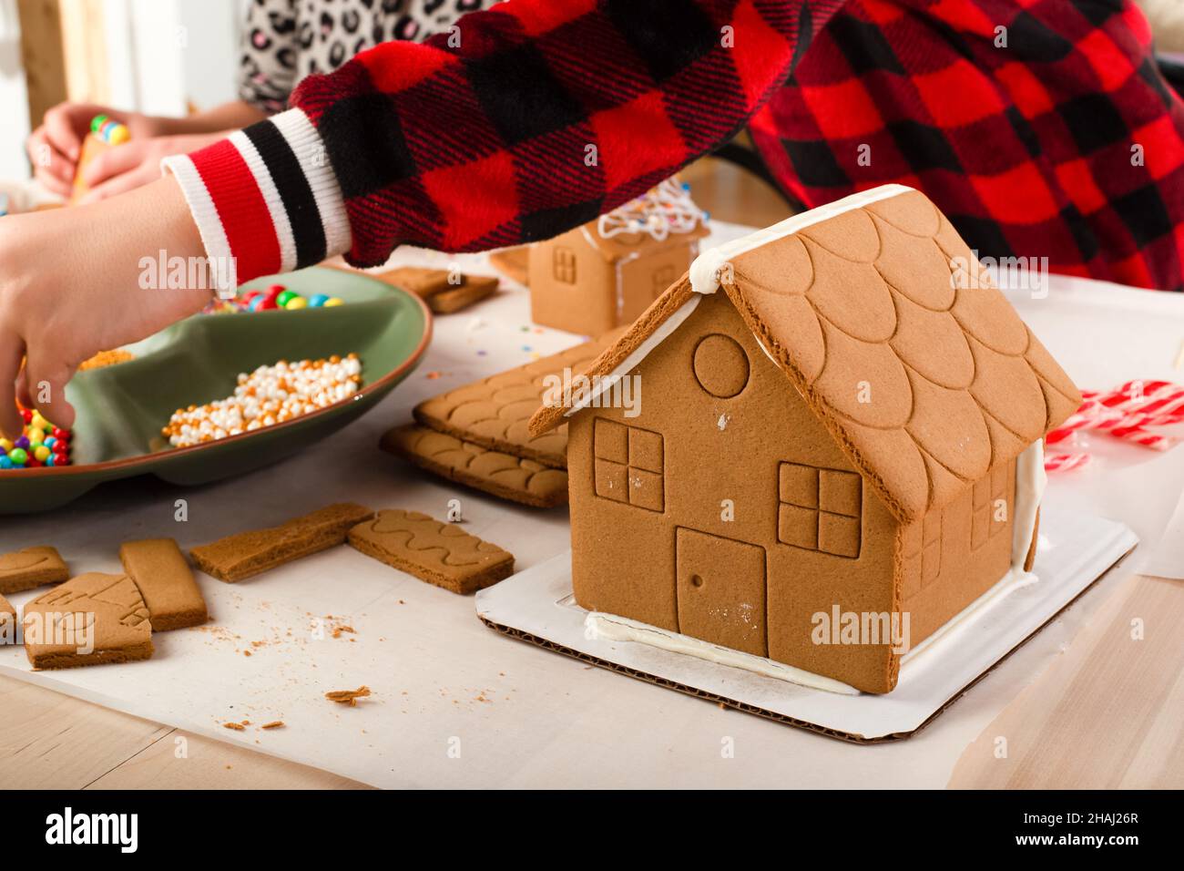 I bambini che assemblano e decorano una casa di pan di zenzero al tempo di Natale. Tradizione di famiglia di Natale, artigianato di Natale. Foto Stock